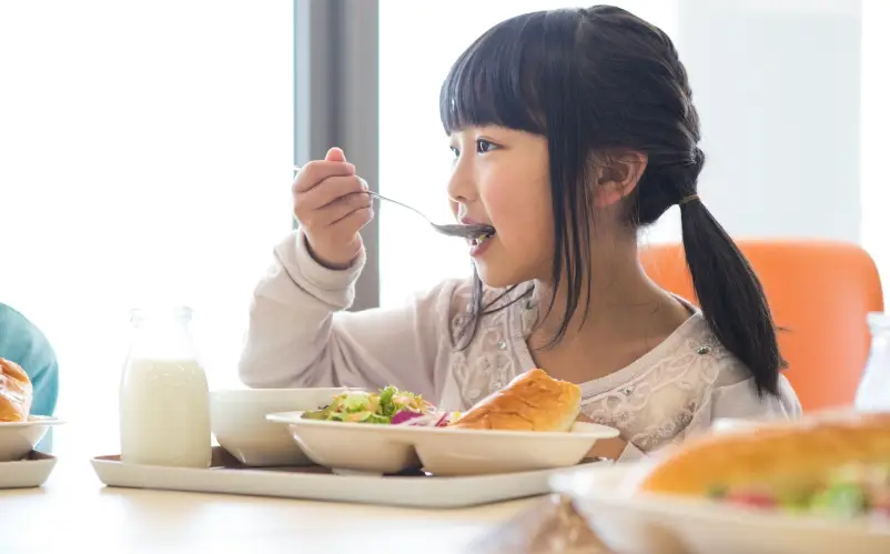 小学生の女の子が給食の時間に食事を楽しんでいる様子